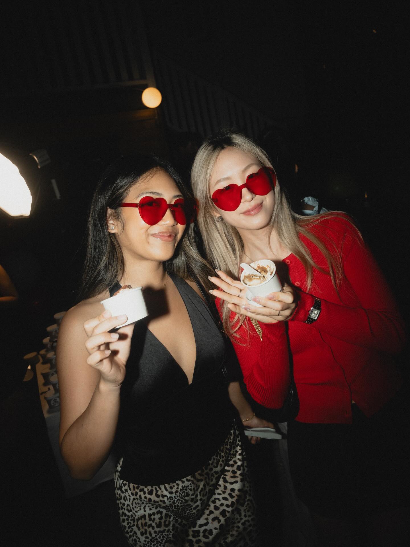 Two guests at the Pick Me Up launch party holding tiramisu cups, wearing red heart glasses